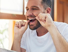 Man smiling while flossing his teeth in bathroom